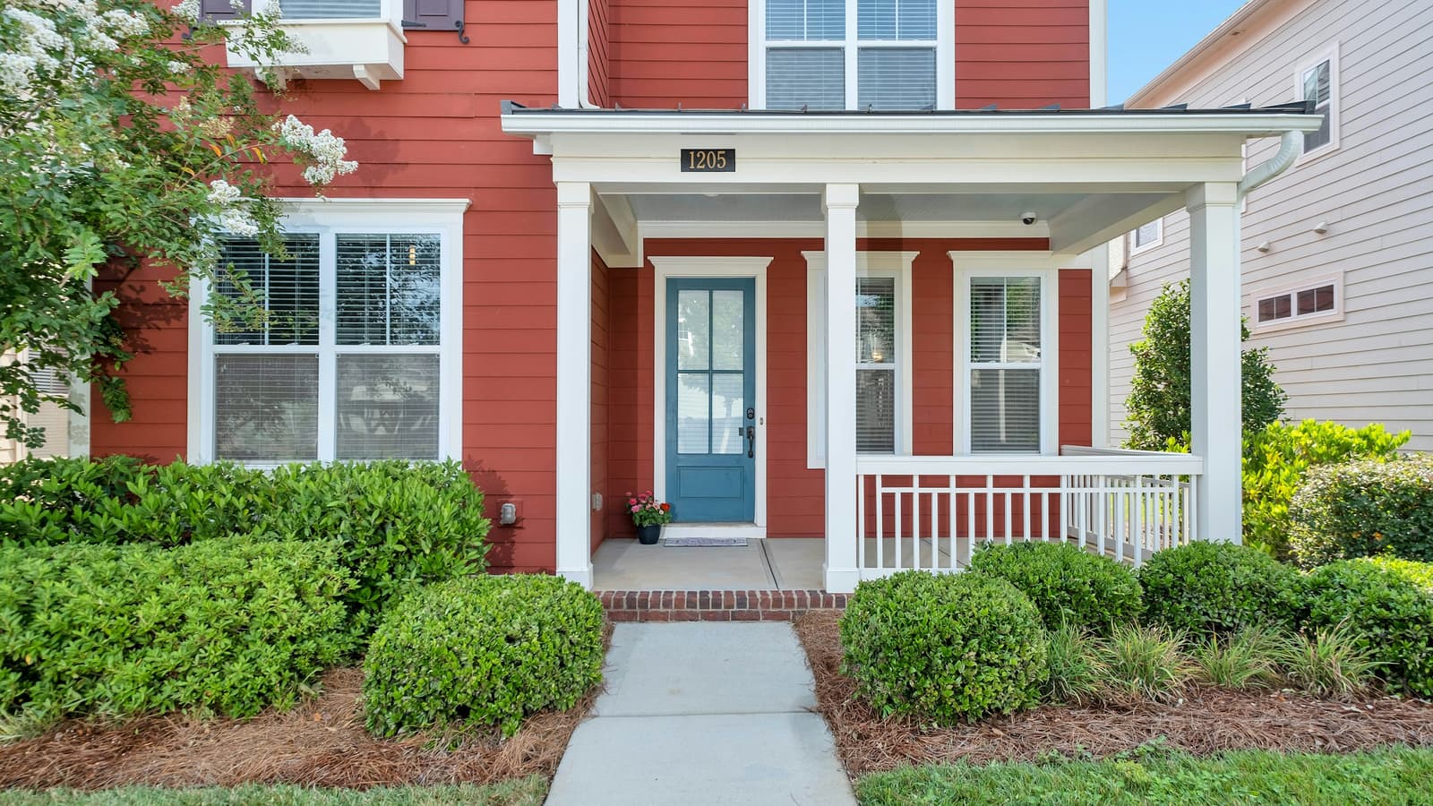 Red craftsman-style house with a front porch, blue door and neatly trimmed shrubs